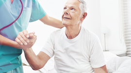 Arzt hilft einem alten Mann, vom Bett aufzustehen