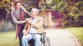Mann im Rollstuhl bei Fahrt durch einen Park mit Betreuerin