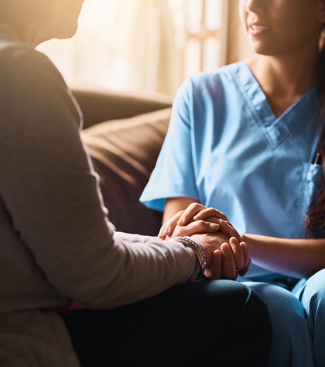 Im Gespr&auml;ch mit einer Seniorin h&auml;lt die junge Pflegerin die H&auml;nde der Seniorin