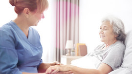 Eine Pflegerin h&auml;lt die Hand einer &auml;lteren, pflegebed&uuml;rftigen Frau im Bett