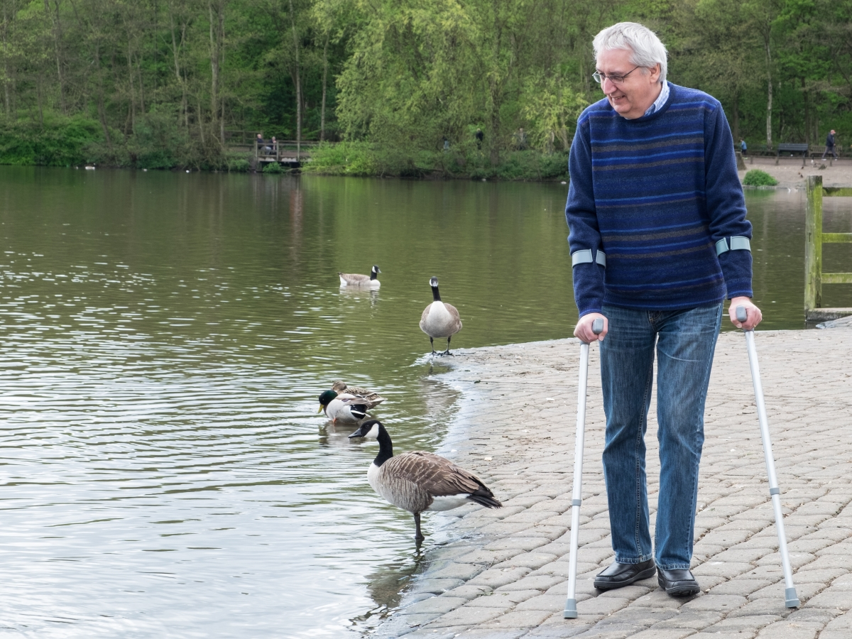 Mann geht mit Kr&uuml;cken am See entlang