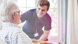 Junger Mann beugt sich zu einem &auml;lteren hinunter, fr&ouml;hliche Situation