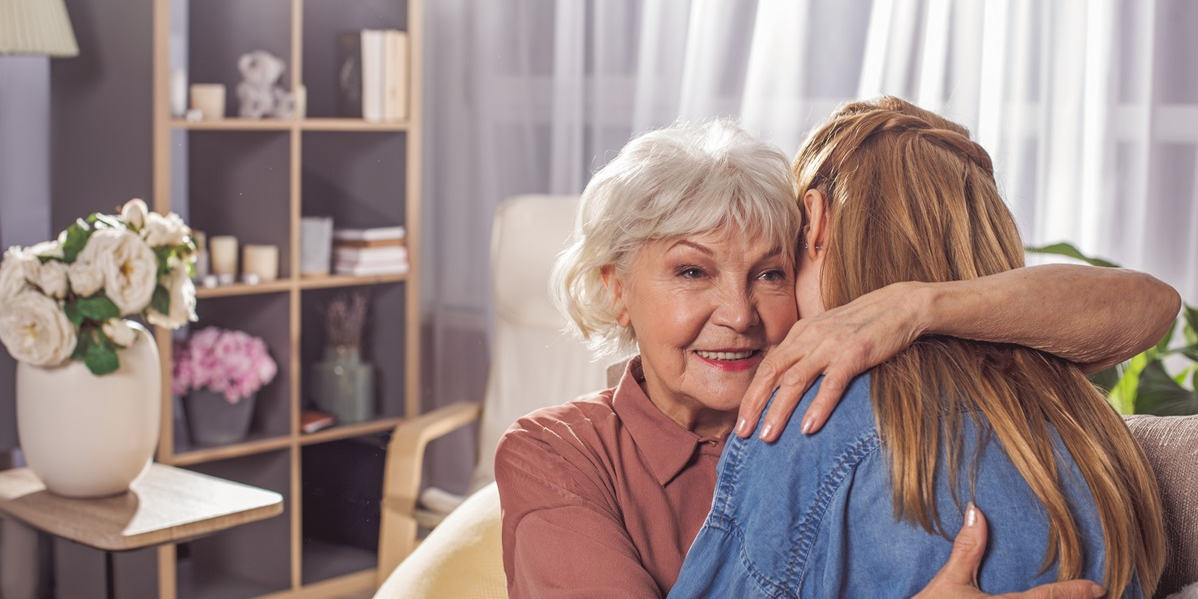 Junge Frau umarmt &auml;ltere Frau im h&auml;uslichen Umfeld