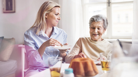 J&uuml;ngere Frau im Gespr&auml;ch mit einer &auml;lteren bei Limonade und Kuchen