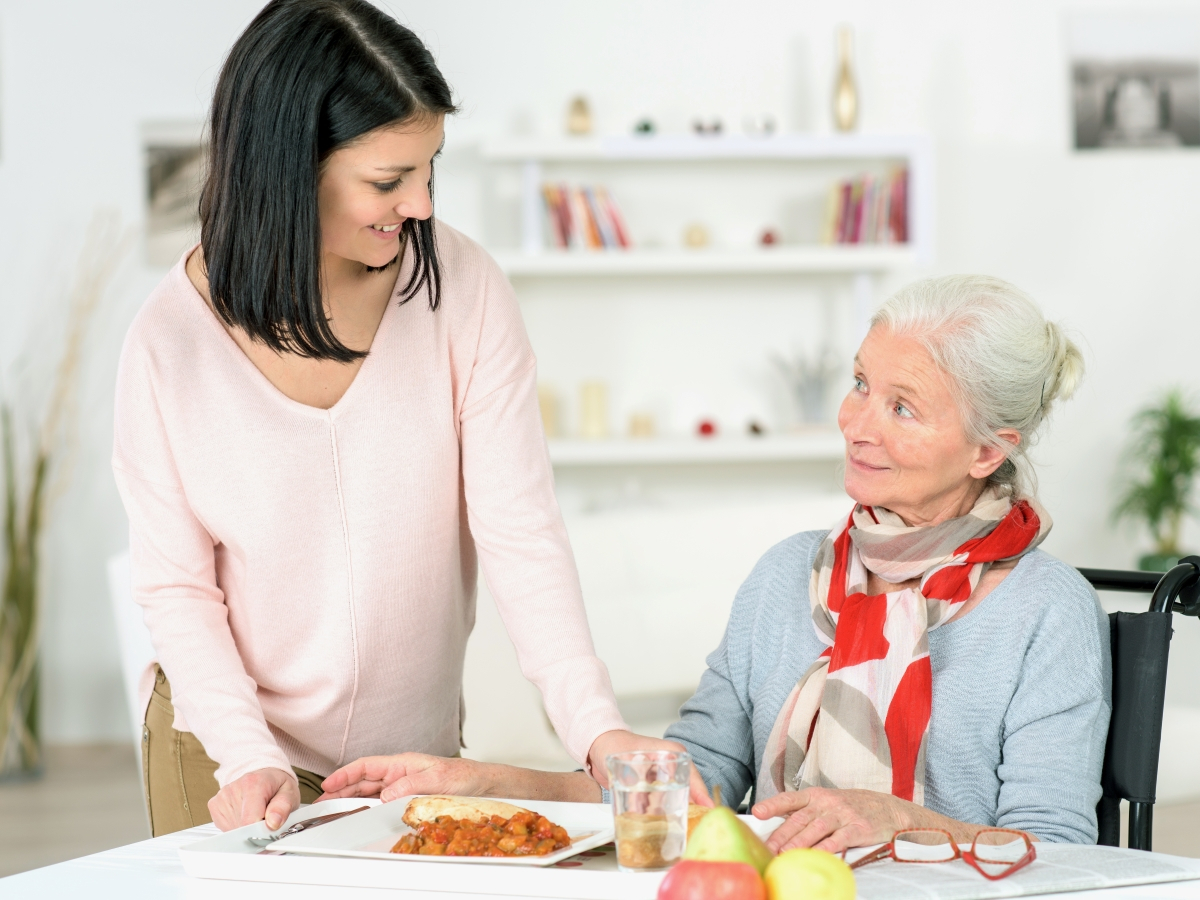 &Auml;ltere Frau am Fr&uuml;hst&uuml;ckstisch, die von einer Pflegerin betreut wird